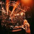 DJ actuando en el escenario con luces cálidas y público