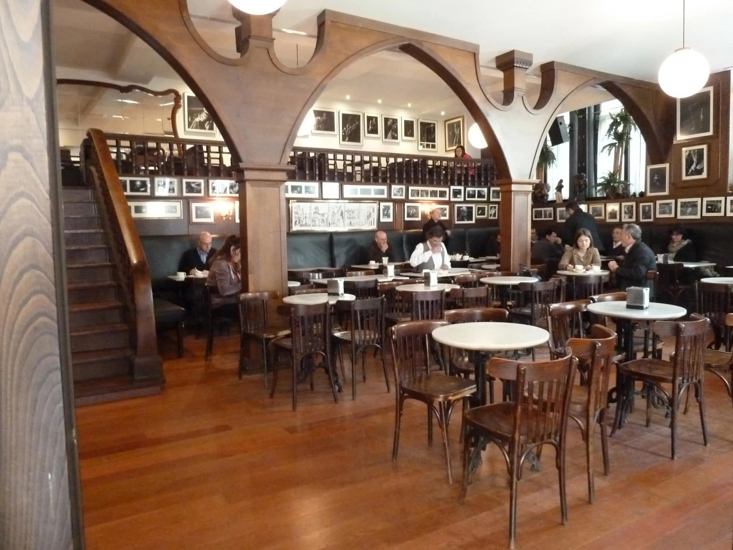 Interior del Café Latino con mesas, sillas y escalera de madera