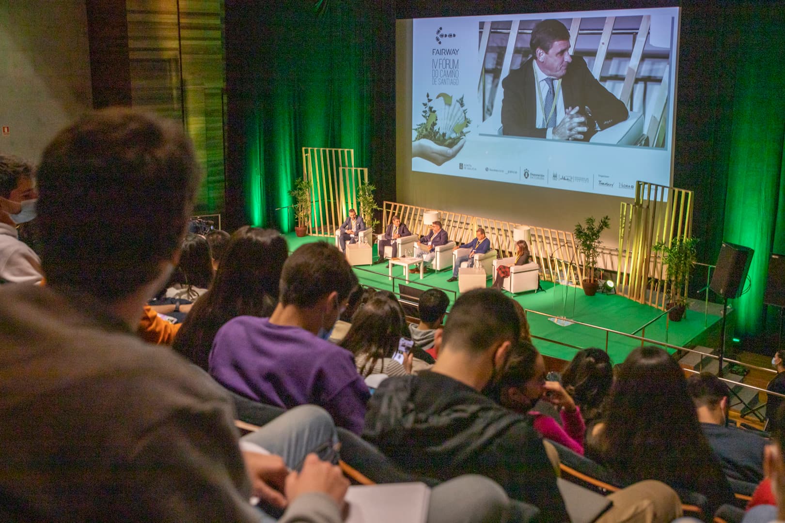 Vista del auditorio desde las butacas con escenario iluminado en verde y pantalla de proyección
